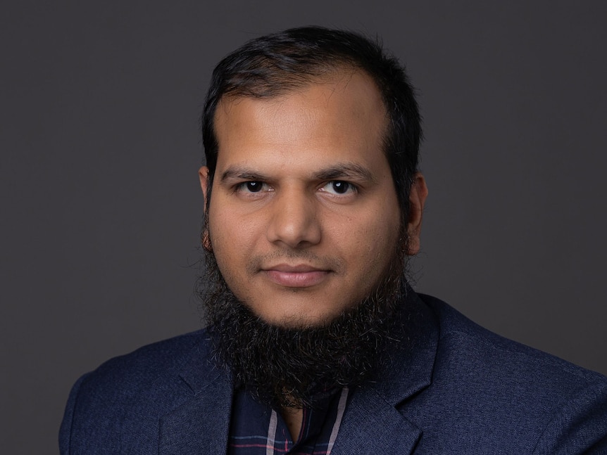 a man with black hair and beard looks to the camera