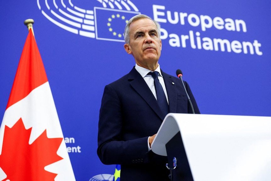 Mark Carney next to a Canadian flag, with 'European Parliament' sign behind him.