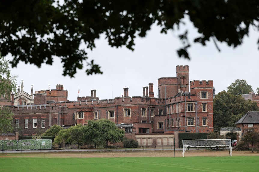 An old brick building sits behind a green soccer field.