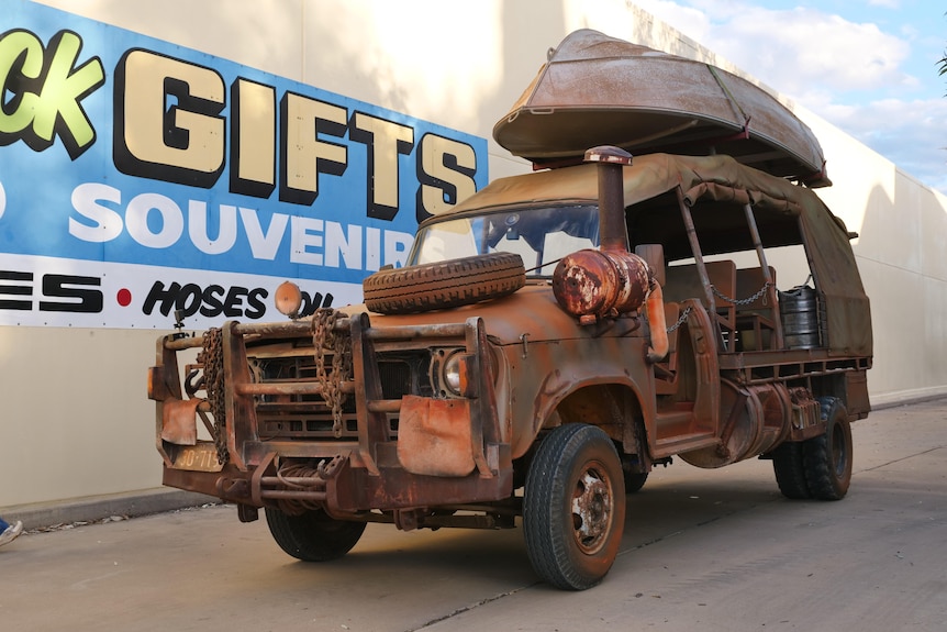 Old safari truck is covered in rust and has a tinny attached to the roof.