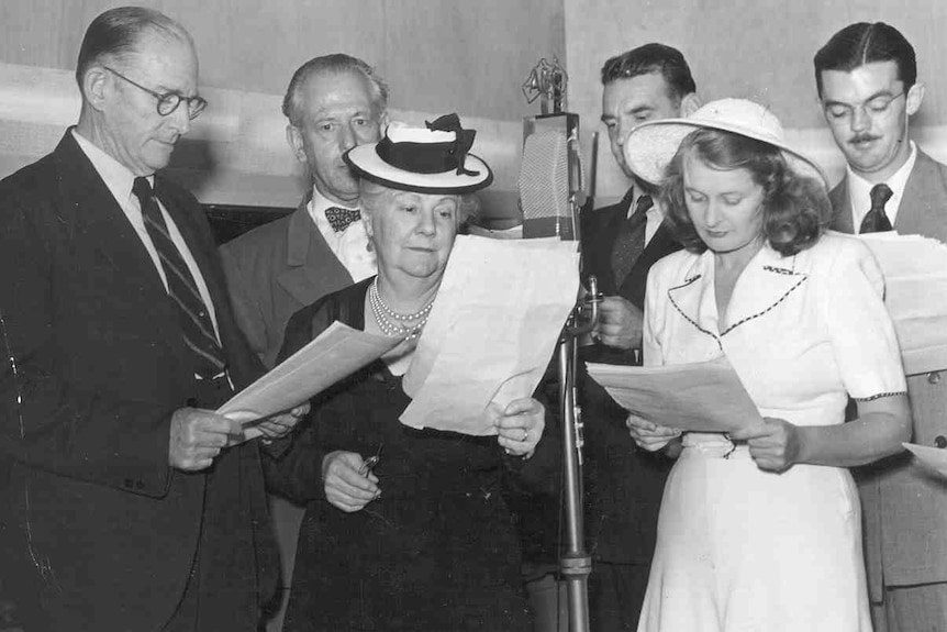 Black and white photo from the 1950s showing voice actors standing around a microphone in a recording studio with scripts