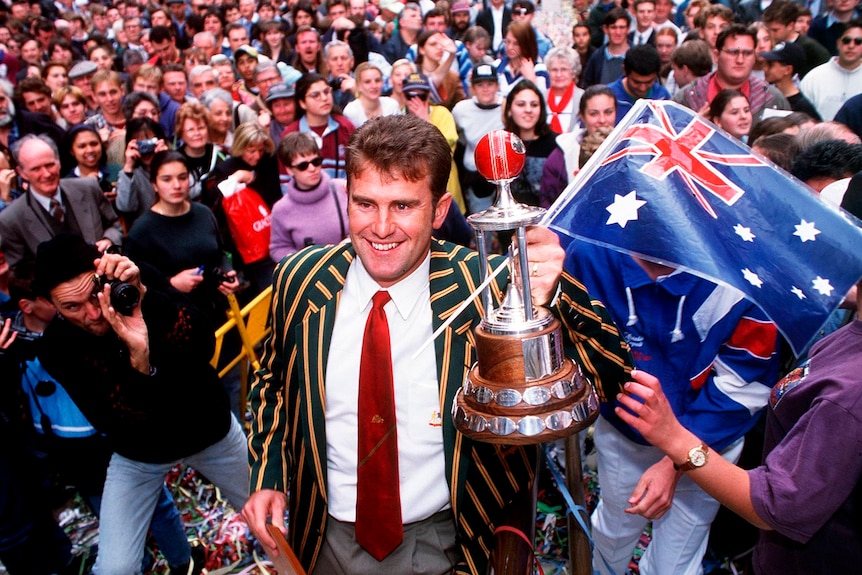Mark Taylor holds trophy during tickertape parade with Australia flag