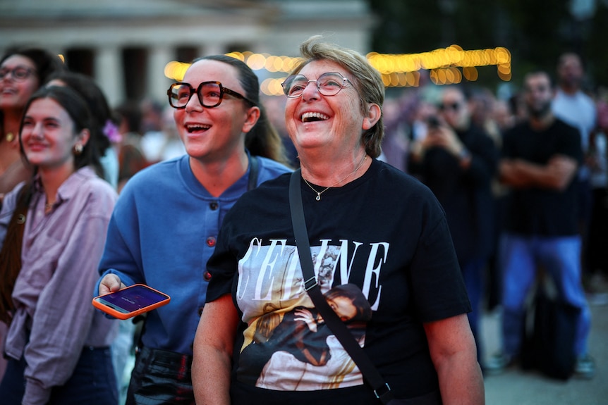 Two women in celine dion t shirts smile as they watch the karaoke