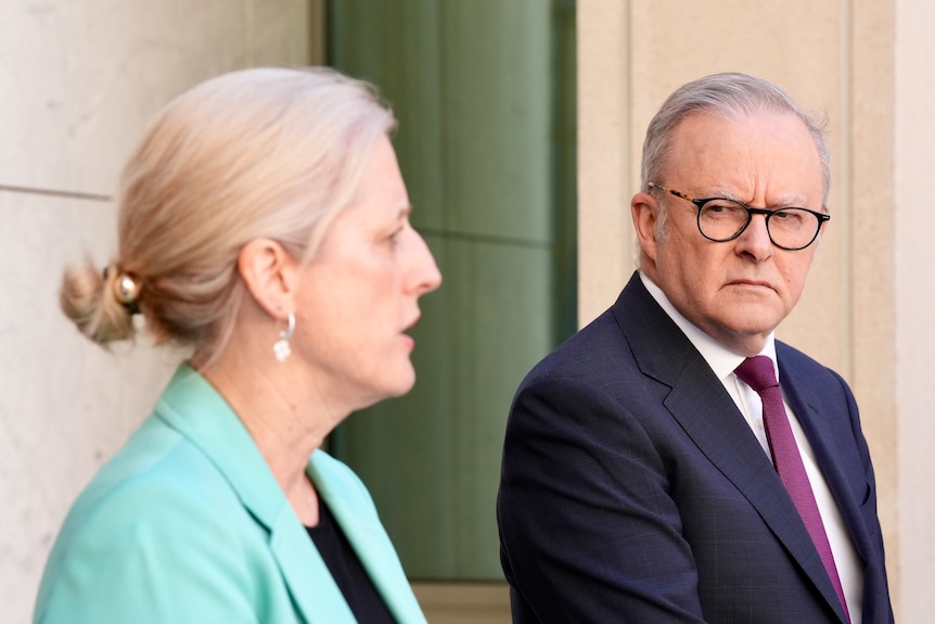 Albanese looks across towards Gallagher, who is speaking out of focus in foreground.
