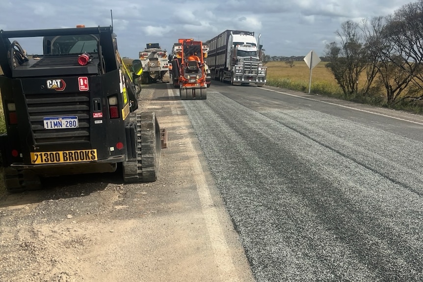 A semitrailer passes machinery on a stretch of country road.