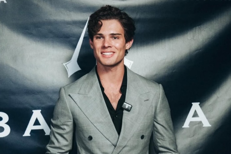 Braden Eric Peters wears a grey suit on a red carpet.