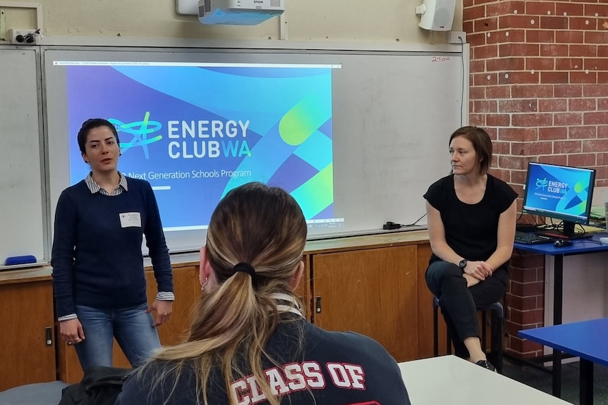 A woman standing in front of a screen that reads "Energy Club WA" speaks in front of a student and teacher.