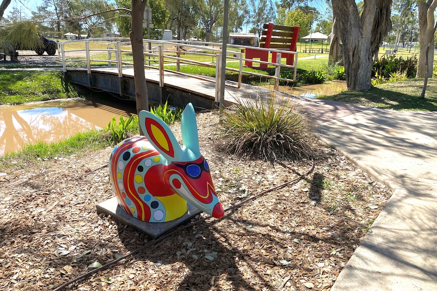 a bilby with painted sunglasses positioned on mulch by a river footbridge