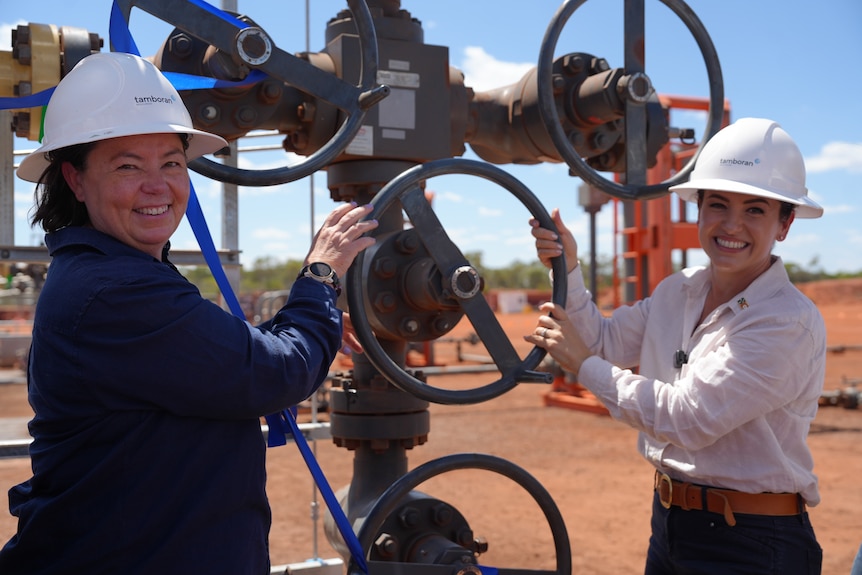 Two female government ministers in hard hats holding a gas tap on a mine site and smiling widely.