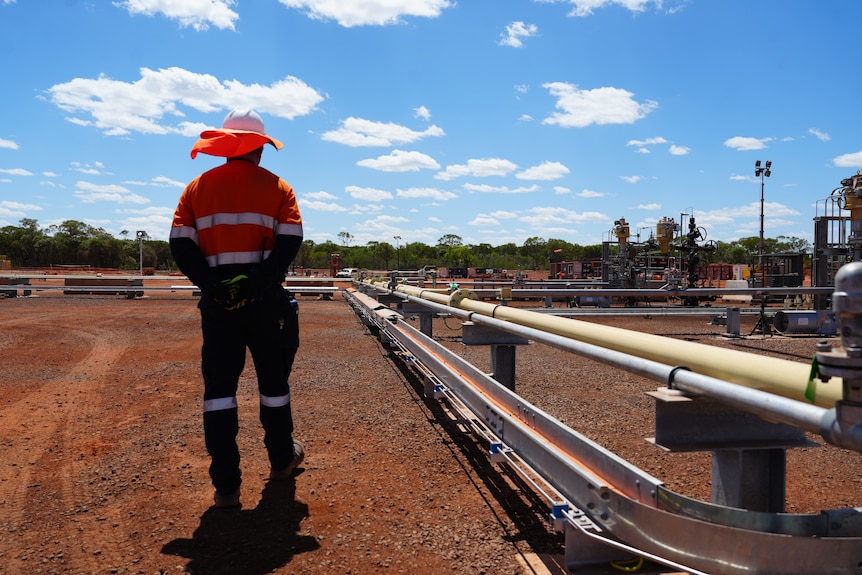 A mine worker in high vis standing beside pipes part of a remote mine site.