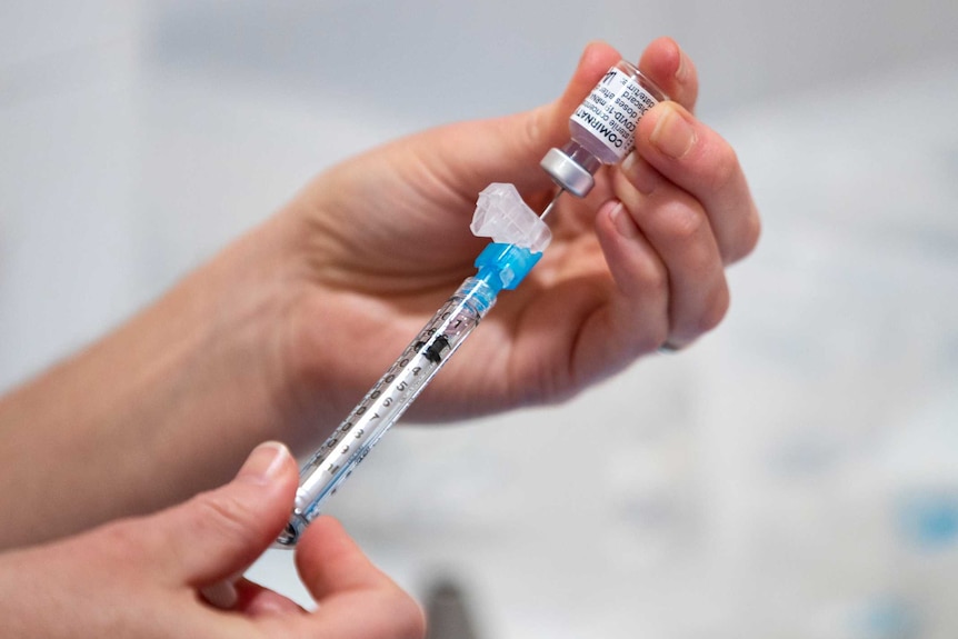 A person inserts a needle into a dose of Pfizer vaccine.