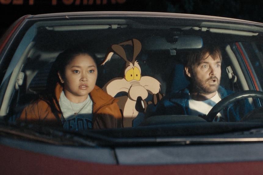 Two people and a cartoon Wile E Coyote sit in a car looking shocked
