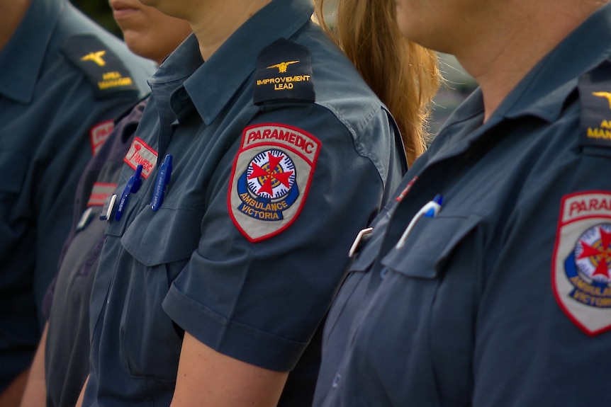 A close up image of three paramedics from the shoulders down with the Ambulance Victoria badge on their sleeves.