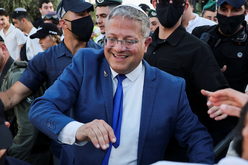 A man in a blue suit and tie walks amongst a busy crowd.
