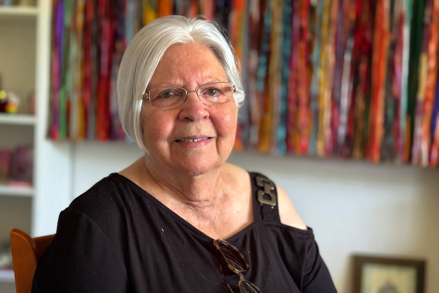 An older lady with short white hair, wearing glasses, and smiling at the camera.