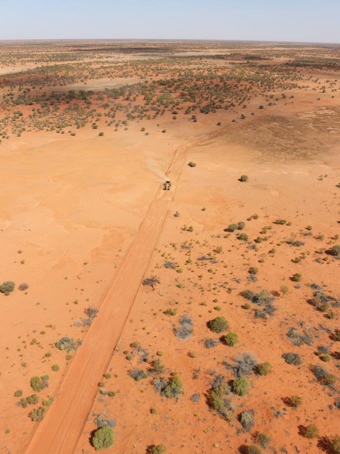An aerial view of land cleared for a fence through red dirt.