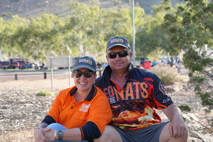 Couple with cap and sunglasses on sit down next to road smiling 