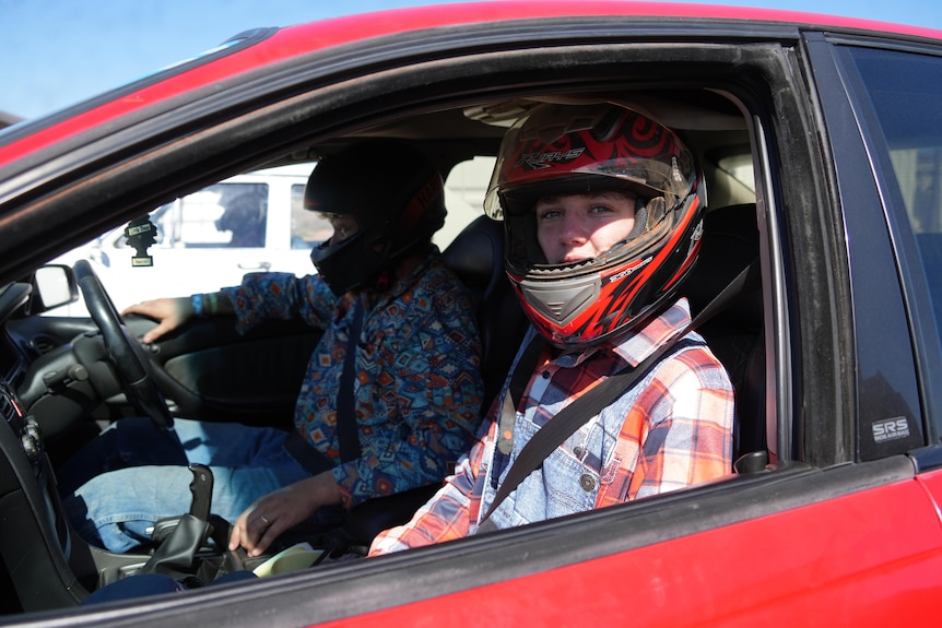 Two men with helmets on in front seats of car  