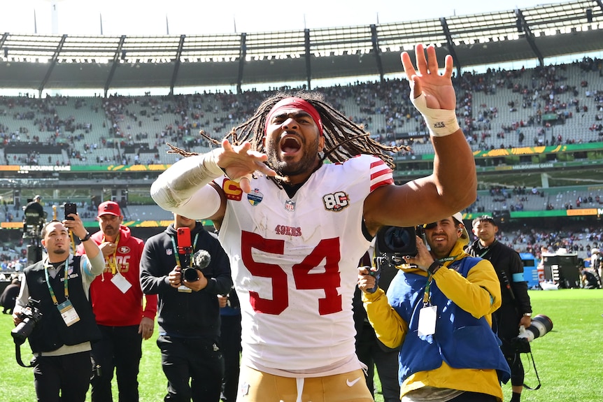 Fred Warner celebrates with both arms raised ahead of photographers