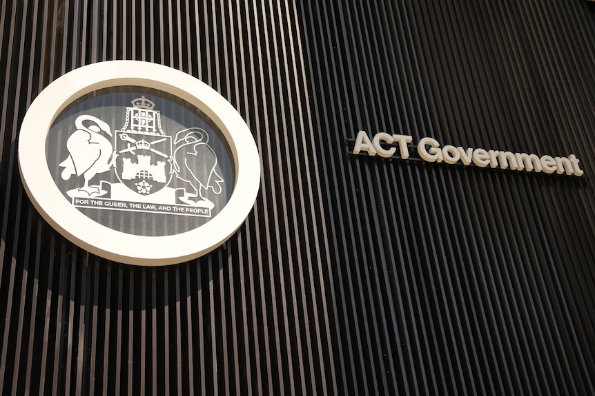 The glass door of a government building with a coat of arms on the left and the words 'ACT government' on the right.