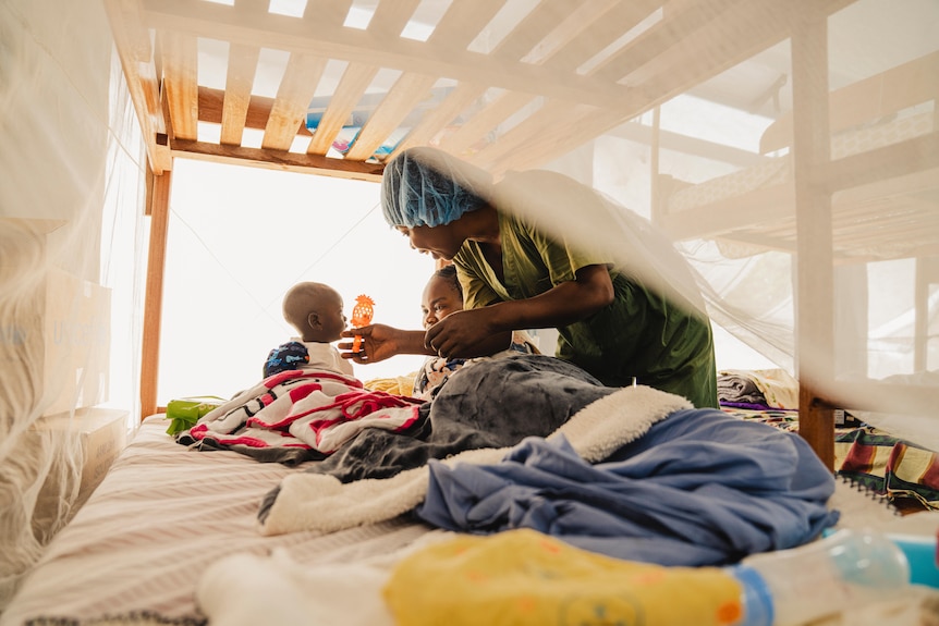 a woman in scrubs reaches for a child on a bed