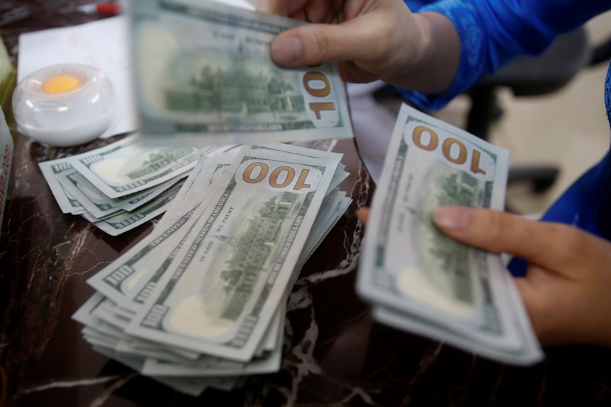 The hands of a person counting through piles of $100 US dollar notes