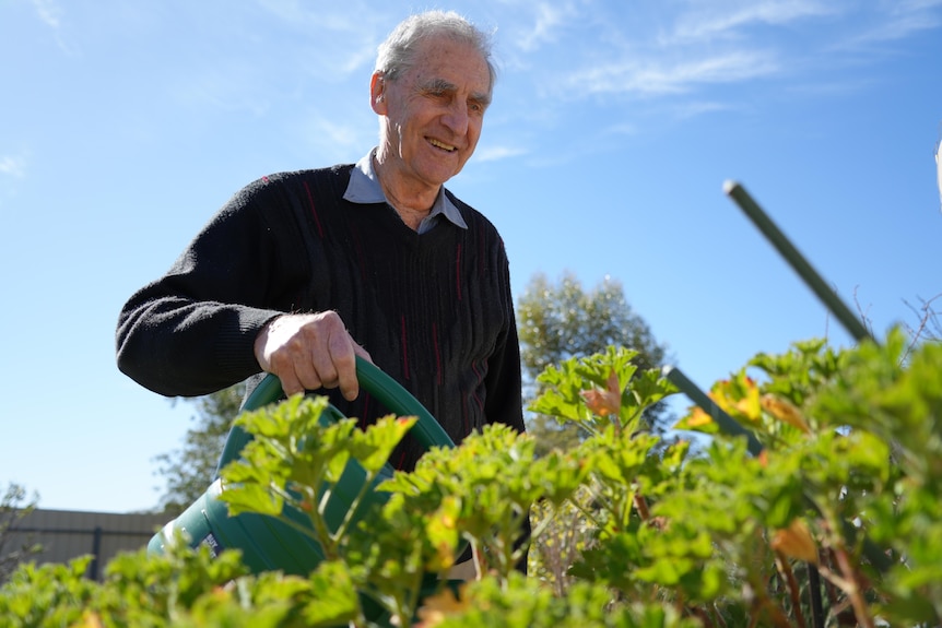 man smiles while watering plants