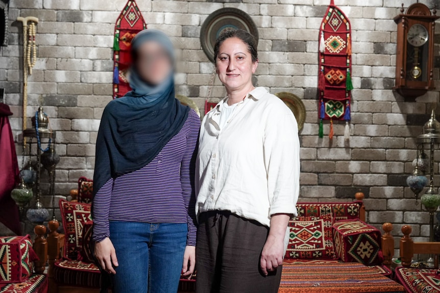 Janna is a petite teenager, her face is blurred. She is next to mum Roula. Behind them are bright textiles.