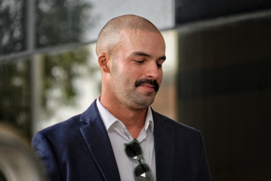 A man in a blazer walking, looking down