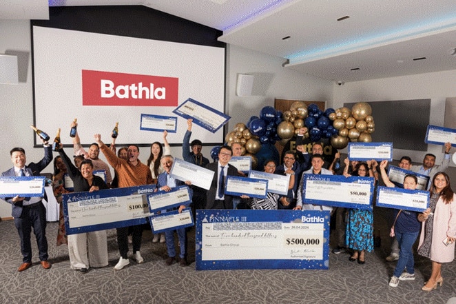 A large group of people smiling with giant cheques, and a sign saying Bathla.