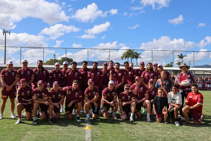 A football team in maroon pose for a team photo on a field