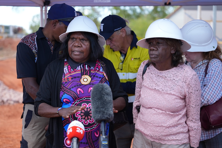 Two women in hard hats standing in front of media microphones at a press conference.