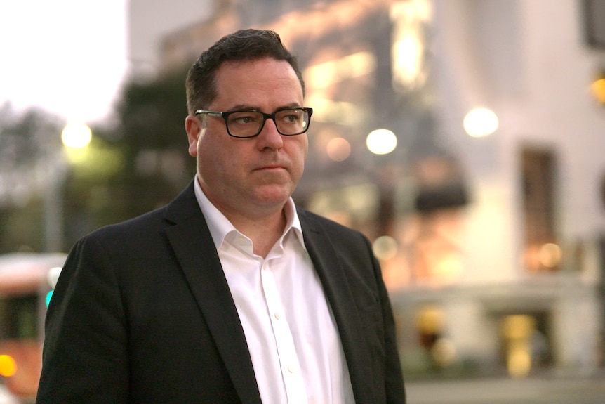 a middle-aged man wearing a white shirt and blazer on a street