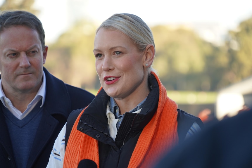 Woman with orange scarf addresses reporters at a press conference.