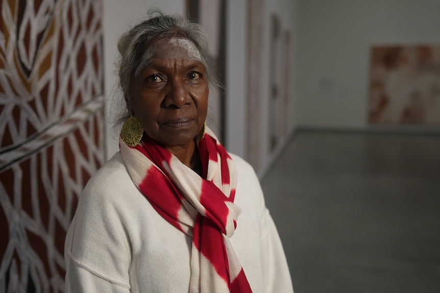 Merrkiyawuy is looking at the camera wearing a white top with a white and red scarf. She has white ochre painted on her forehead