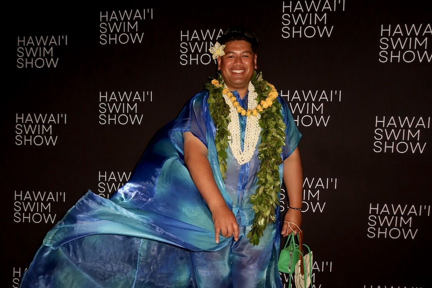 A man wearing flowy blue clothes and flowers on a red carpet.
