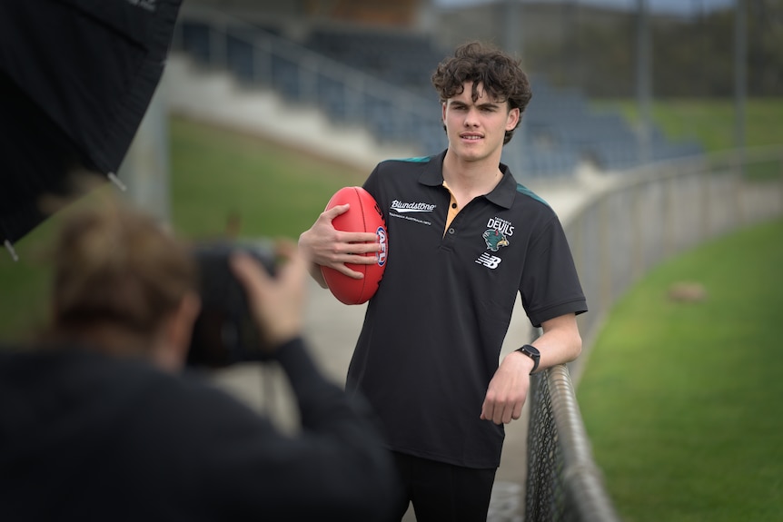 Hugh McCallum leaning on a fence while holding a football posing for a photo