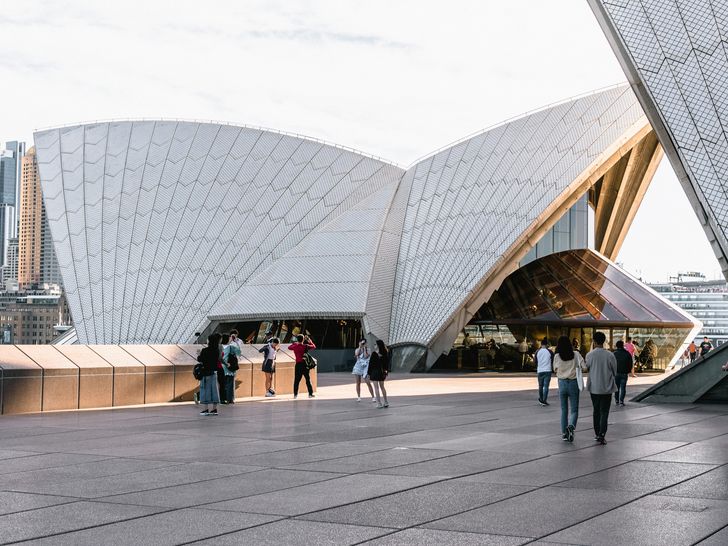 People enjoying the Opera House forecourt from a streetscape level, surrounded by the building’s iconic shell-like roof form.