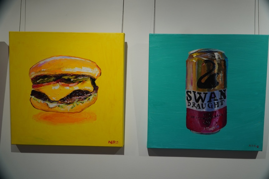A painting of a cheeseburger against a yellow background and a lager can against a blue background hang in a gallery