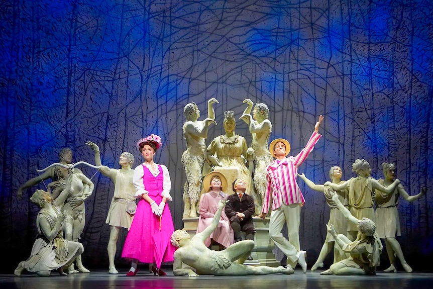 An image of a stage performance of Mary Poppins in the Park, with Mary, Burt, Jane and Michael, and several grey statues.