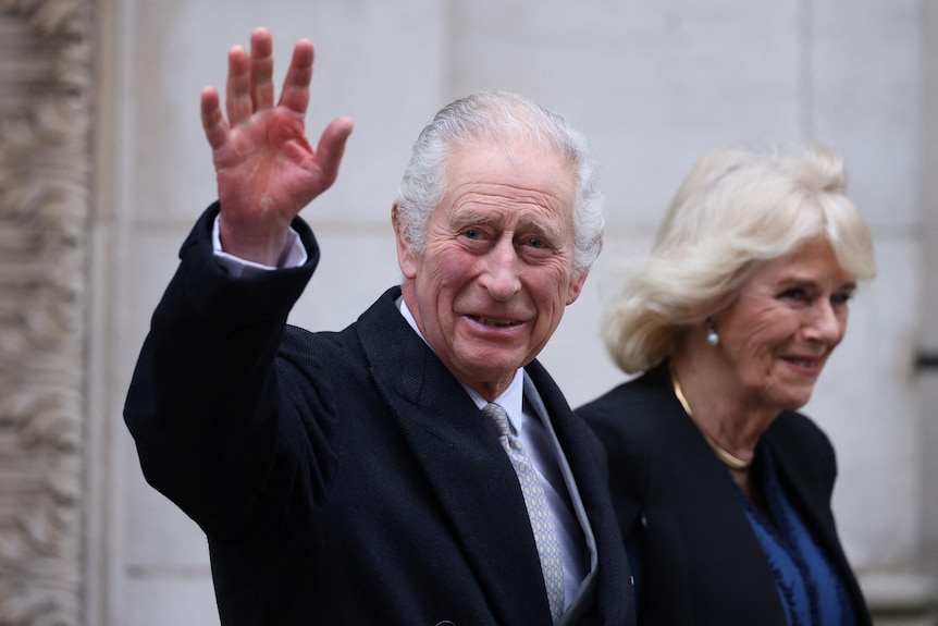King Charles waves as he walks alongside Queen Camilla