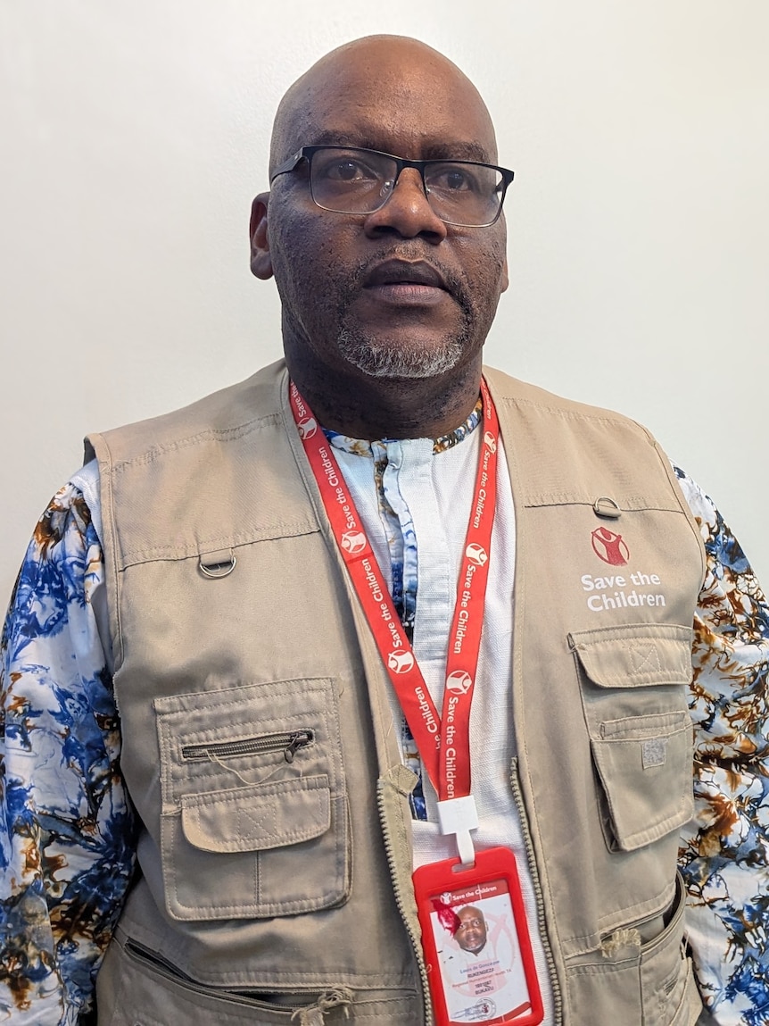 a man in a vest stands against a white background 