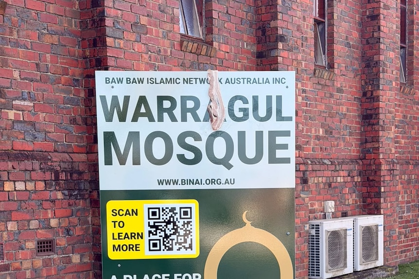 A rasher of bacon hangs over a sign that says "Warragul Mosque" in front of a brick building.