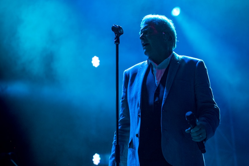 John Farnham behind a mic with smoky air and lights.