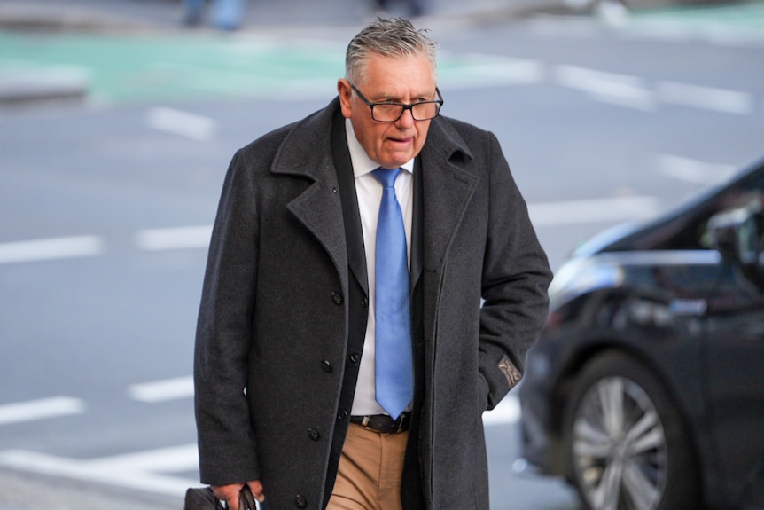 Man in a suit and jacket with glasses walks in street