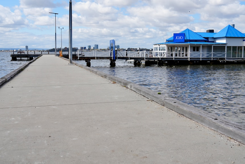 A concrete jetty in a river that leads to a white building with a bright blue roof and a sign that reads JoJo's.