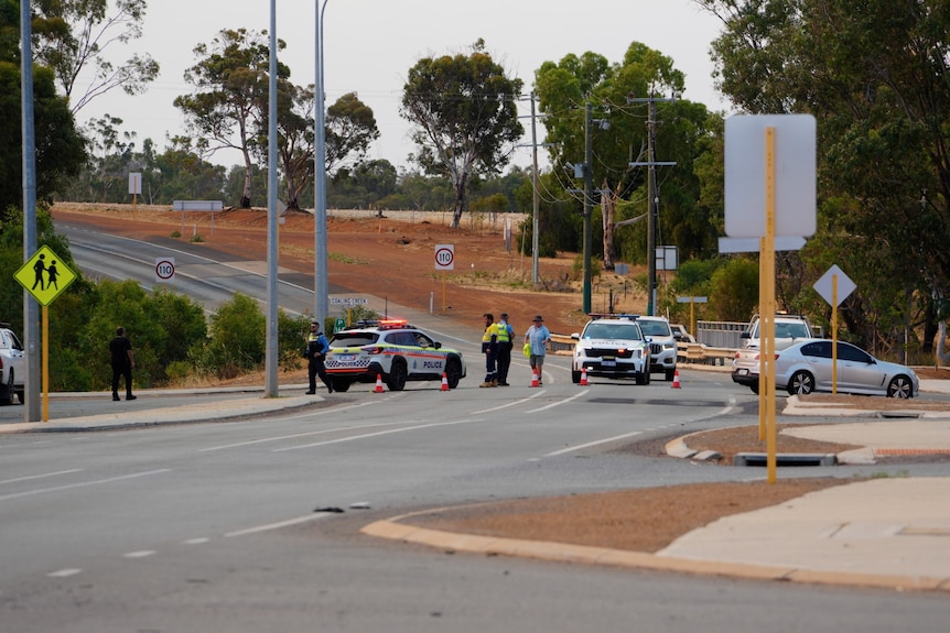 Police officers and cars block a road at the entry to a town in WA