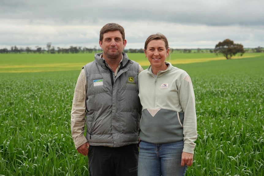 A man and woman stand in front of green paddocks