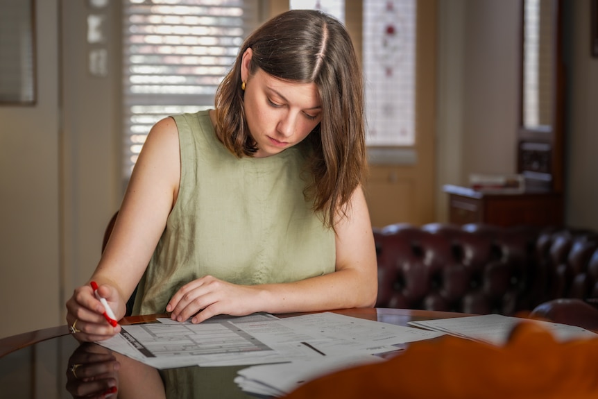 A person sitting at a table reading through documents and holding a red highlighter.