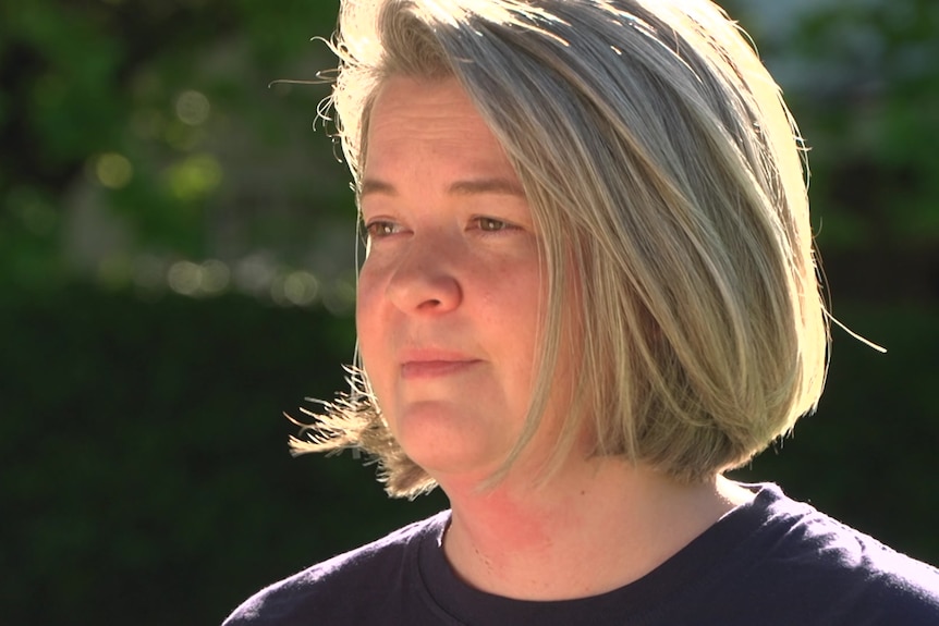 A side profile image of a woman wearing a dark T-Shirt in front of a hedge